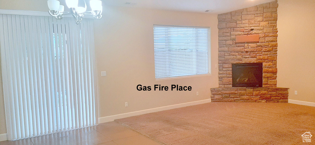 Unfurnished living room with an inviting chandelier, a stone fireplace, lofted ceiling, and tile patterned floors