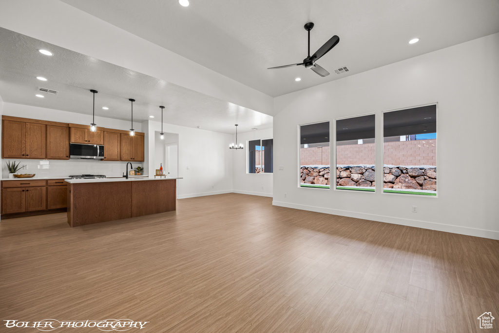 Kitchen with an island with sink, ceiling fan with notable chandelier, light wood-type flooring, decorative light fixtures, and sink