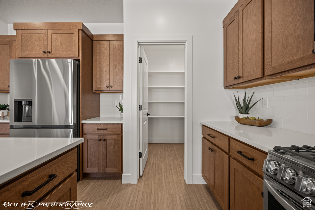 Kitchen with decorative backsplash, light wood-type flooring, and appliances with stainless steel finishes