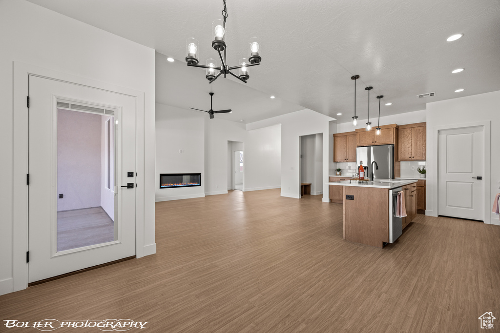 Kitchen featuring a center island with sink, decorative light fixtures, appliances with stainless steel finishes, ceiling fan with notable chandelier, and light hardwood / wood-style floors