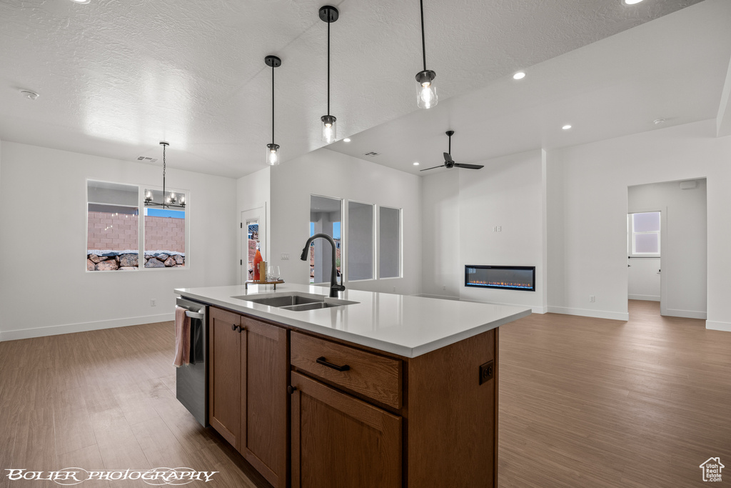 Kitchen featuring light wood-type flooring, a textured ceiling, a kitchen island with sink, and sink