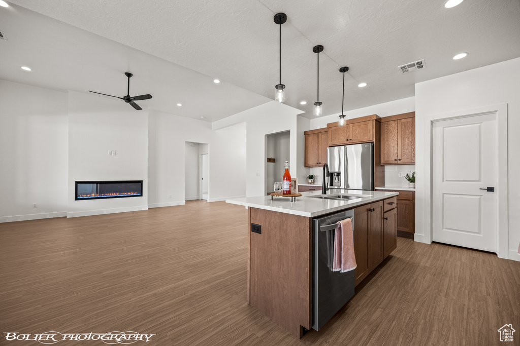 Kitchen with appliances with stainless steel finishes, dark wood-type flooring, pendant lighting, ceiling fan, and a center island with sink