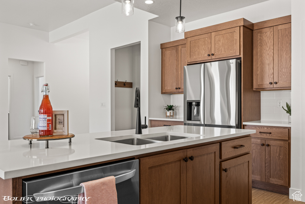 Kitchen featuring light hardwood / wood-style floors, sink, stainless steel appliances, backsplash, and a center island with sink