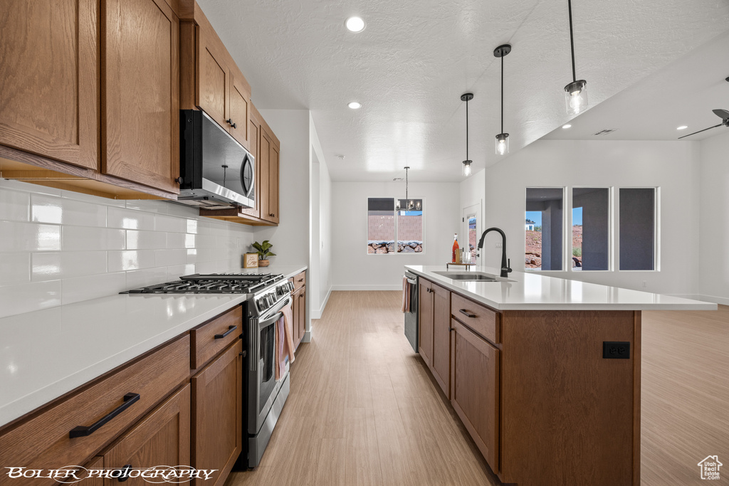 Kitchen with pendant lighting, an island with sink, sink, stainless steel appliances, and light wood-type flooring