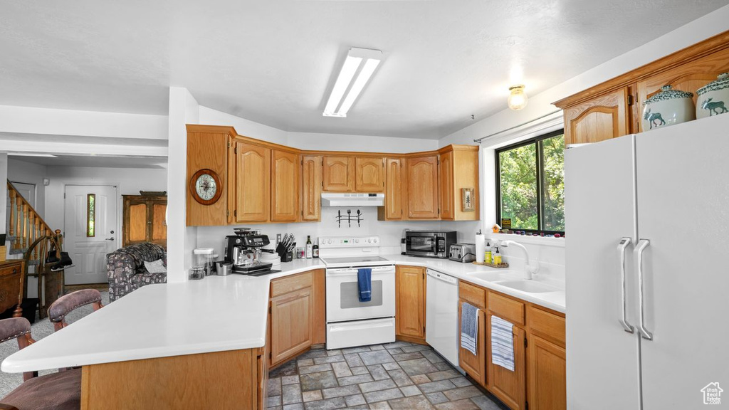 Kitchen featuring kitchen peninsula, a breakfast bar area, sink, white appliances, and light tile floors