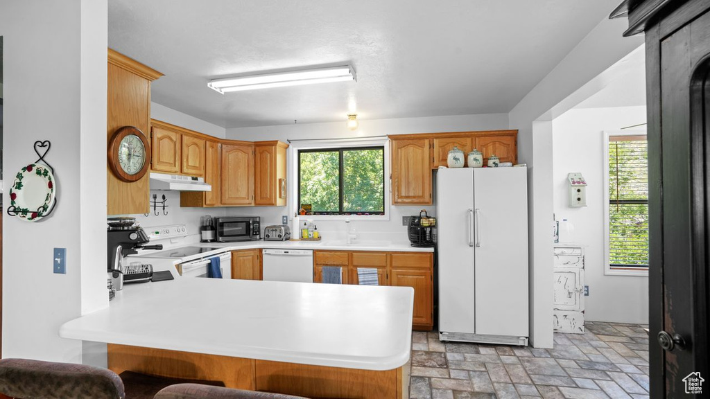 Kitchen with sink, kitchen peninsula, white appliances, and a kitchen bar