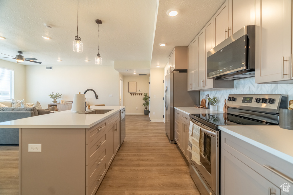 Kitchen featuring appliances with stainless steel finishes, hanging light fixtures, sink, and light hardwood / wood-style flooring