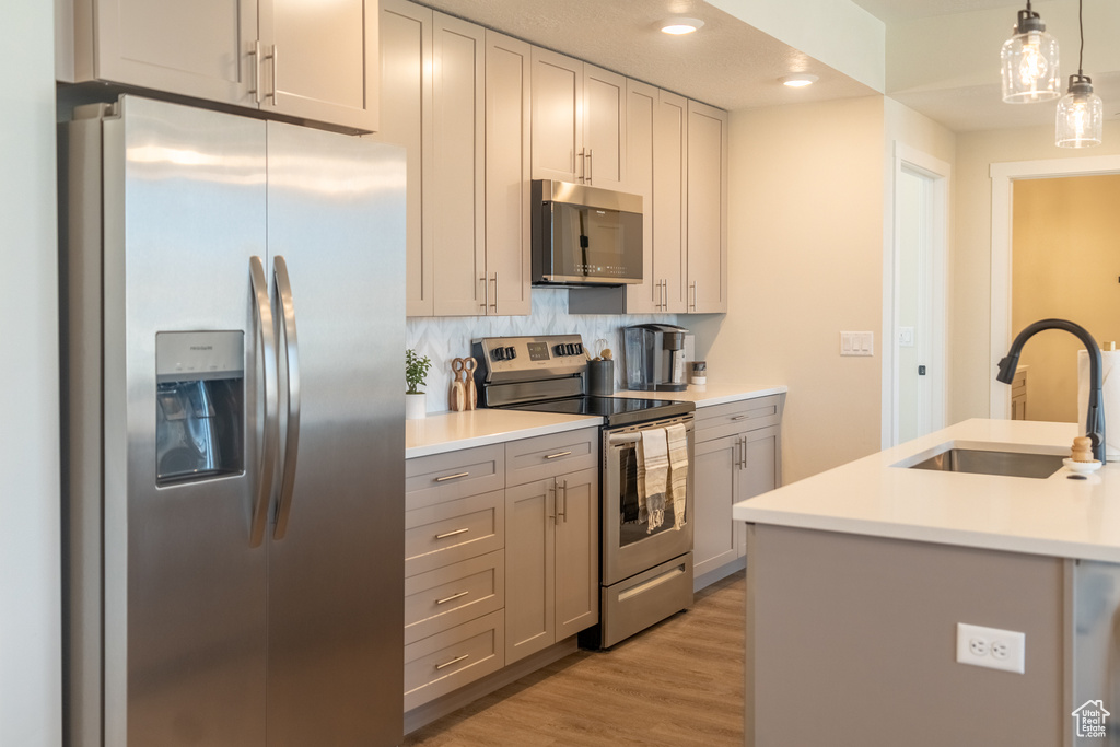 Kitchen featuring light hardwood / wood-style flooring, stainless steel appliances, backsplash, hanging light fixtures, and gray cabinetry