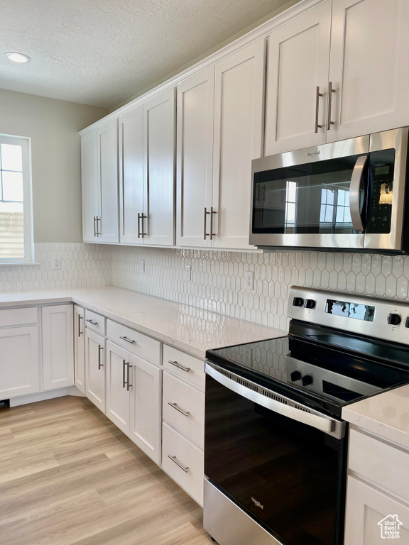 Kitchen with light hardwood / wood-style floors, tasteful backsplash, white cabinetry, and appliances with stainless steel finishes