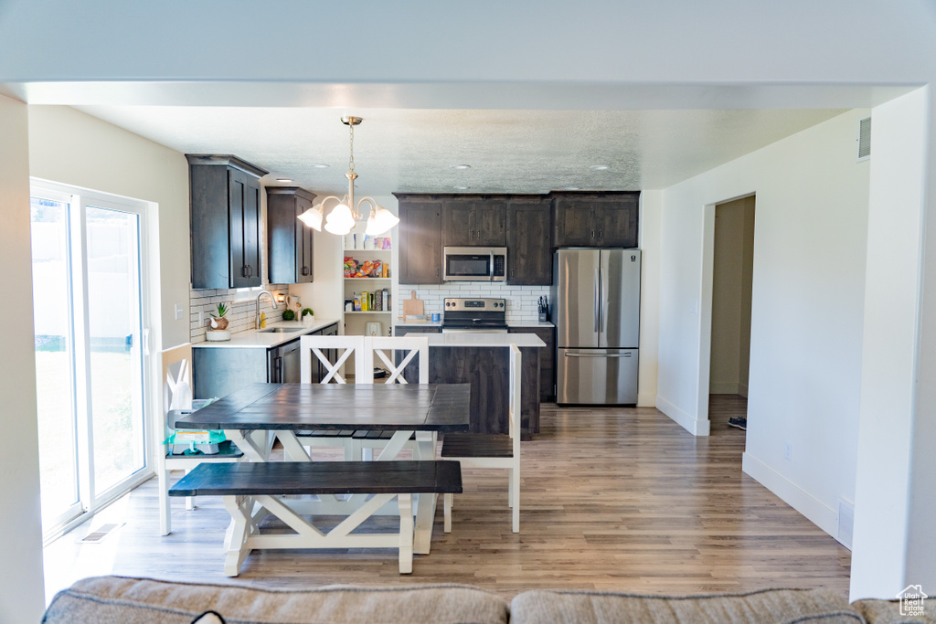 Kitchen featuring tasteful backsplash, pendant lighting, light wood-type flooring, and stainless steel appliances