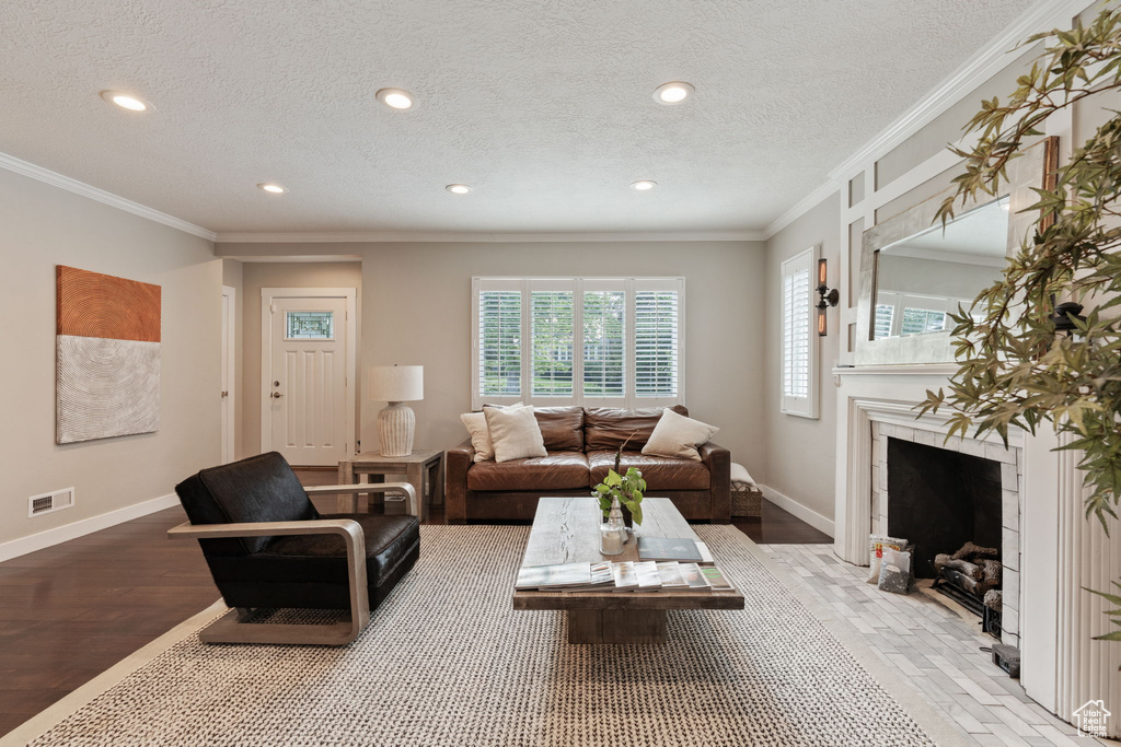 Living room featuring a high end fireplace, hardwood / wood-style flooring, a textured ceiling, and crown molding