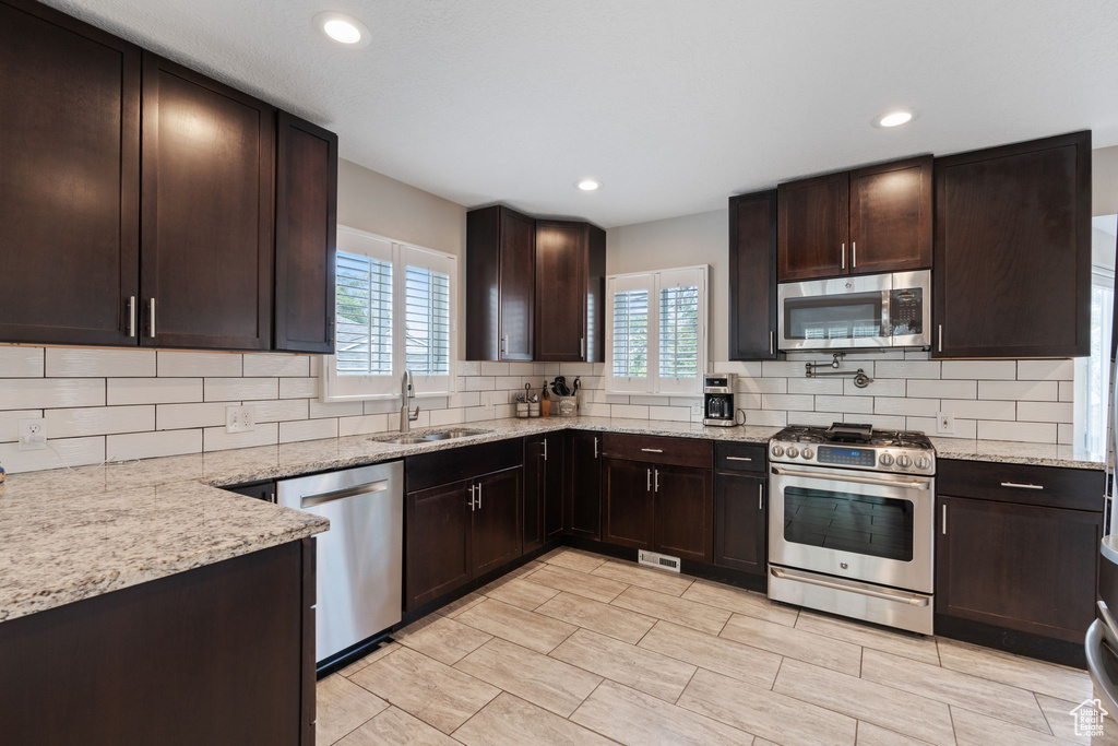 Kitchen with tasteful backsplash, stainless steel appliances, light stone counters, light tile floors, and sink