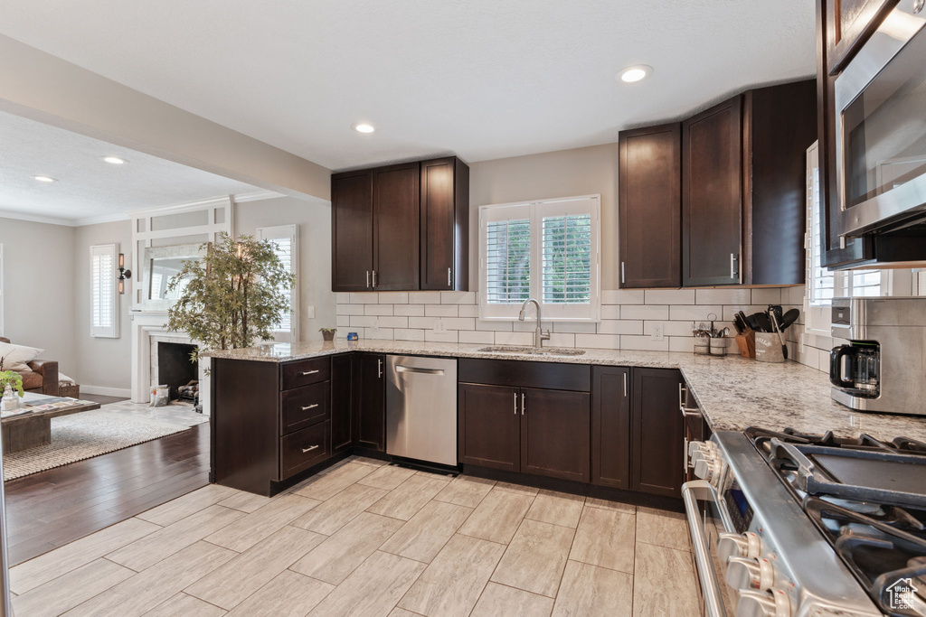 Kitchen with dark brown cabinets, light hardwood / wood-style flooring, backsplash, sink, and appliances with stainless steel finishes