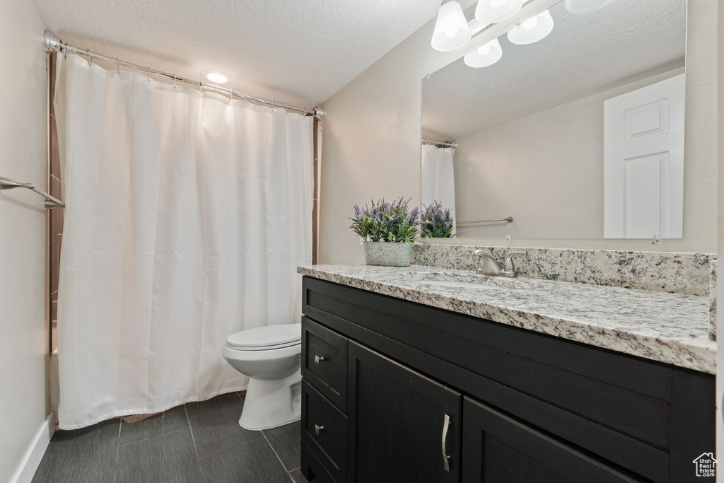 Bathroom with tile floors, a textured ceiling, toilet, and vanity with extensive cabinet space