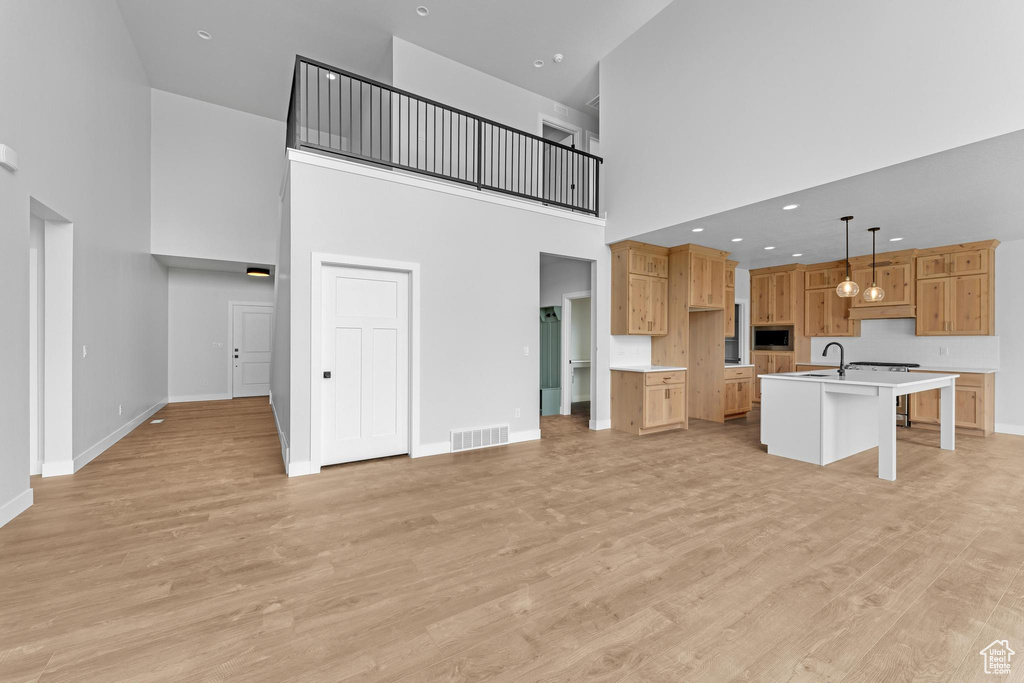 Kitchen featuring a kitchen island with sink, light hardwood / wood-style flooring, hanging light fixtures, a towering ceiling, and stainless steel microwave