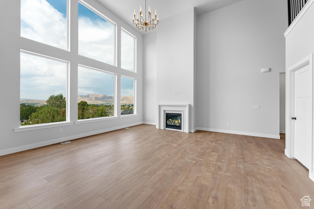 Unfurnished living room with light hardwood / wood-style flooring, a high ceiling, and a notable chandelier