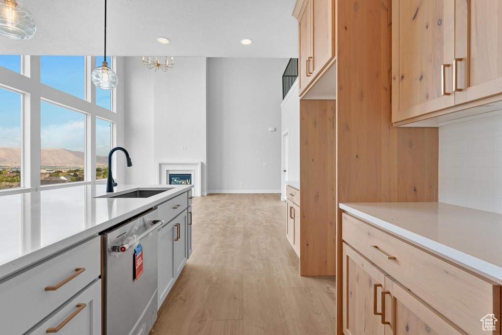 Kitchen with decorative light fixtures, light hardwood / wood-style flooring, light brown cabinetry, stainless steel dishwasher, and sink