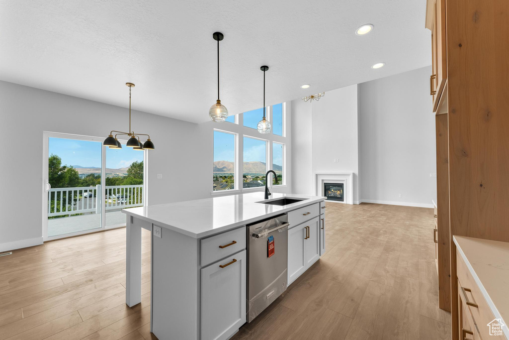 Kitchen with pendant lighting, an island with sink, sink, stainless steel dishwasher, and white cabinets