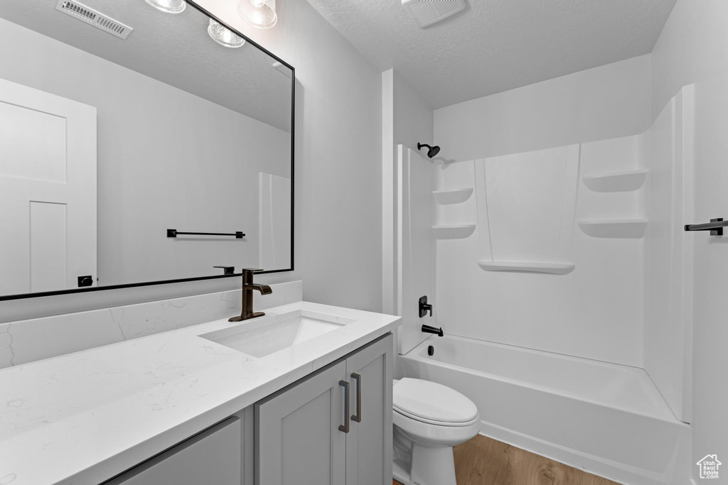 Full bathroom featuring toilet, hardwood / wood-style floors, vanity, a textured ceiling, and tub / shower combination