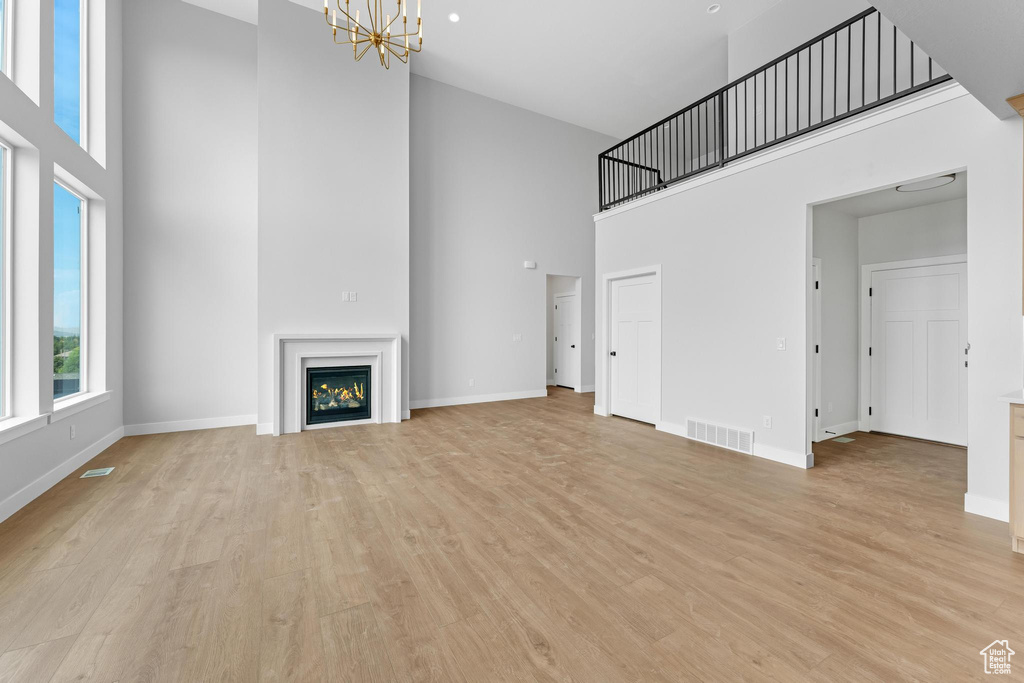 Unfurnished living room with light hardwood / wood-style flooring, a high ceiling, and a notable chandelier