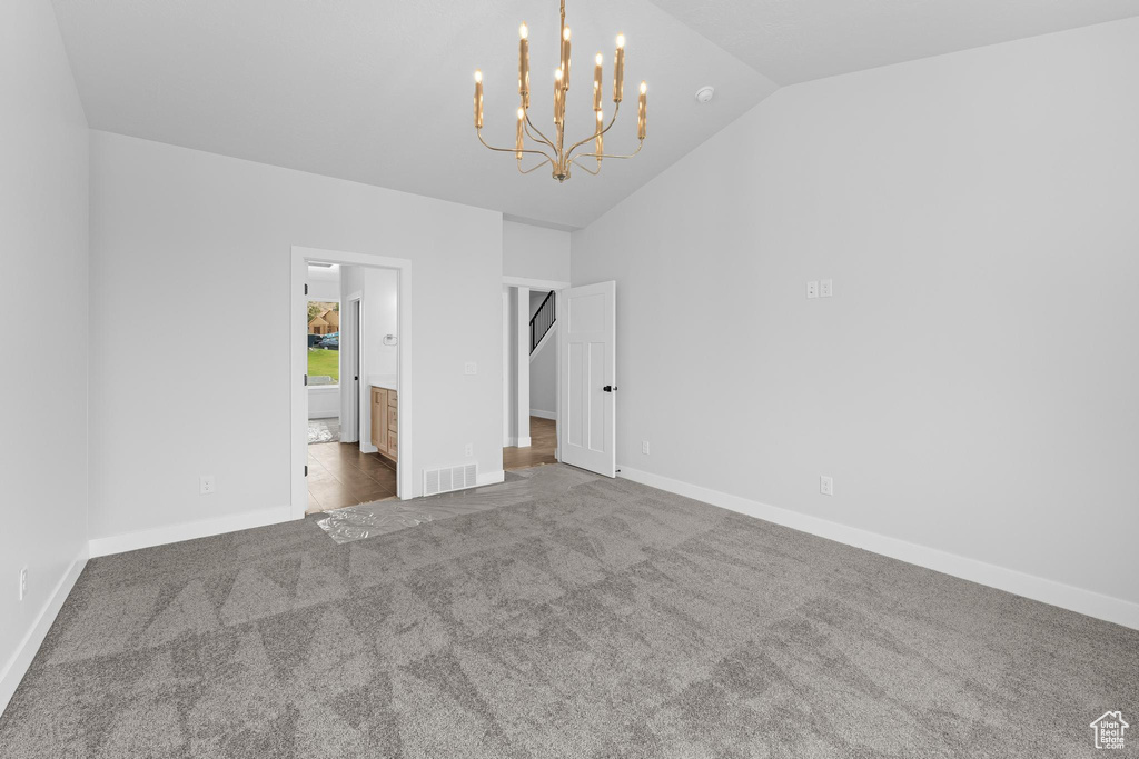 Unfurnished bedroom featuring carpet flooring, connected bathroom, an inviting chandelier, and vaulted ceiling