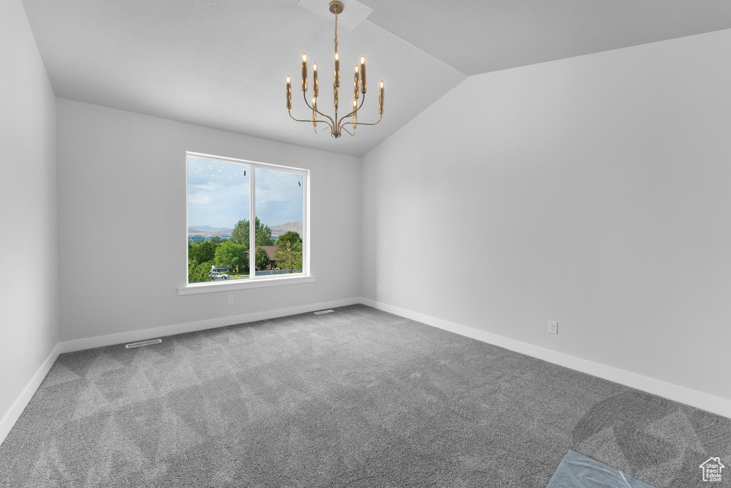 Empty room featuring lofted ceiling, a chandelier, and carpet