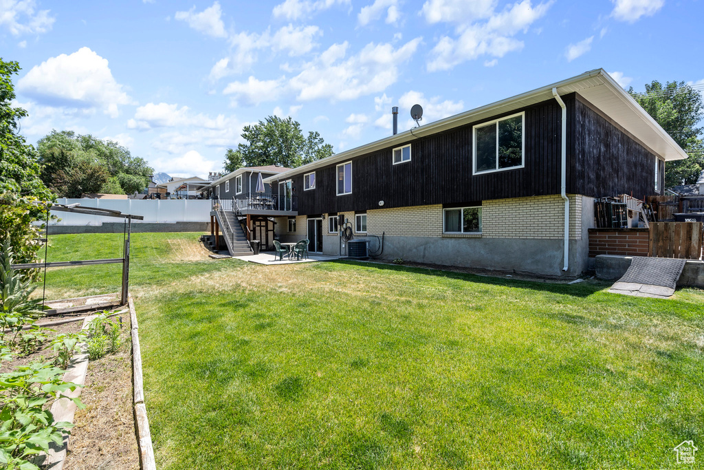 Rear view of house featuring central AC, a wooden deck, and a yard