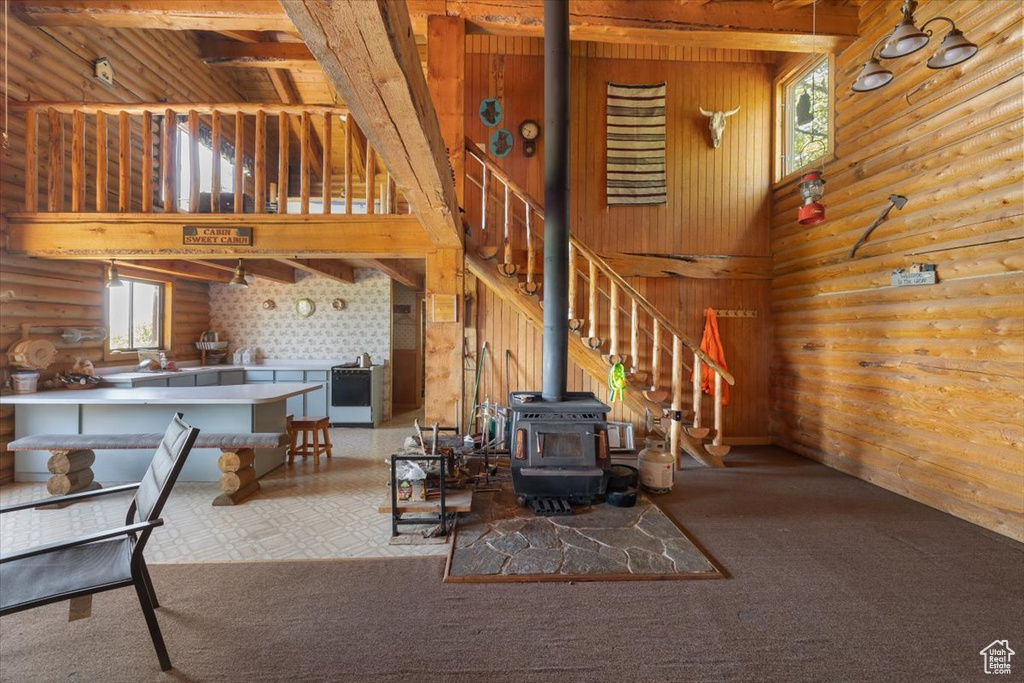 Living room featuring carpet, beam ceiling, log walls, and a wood stove