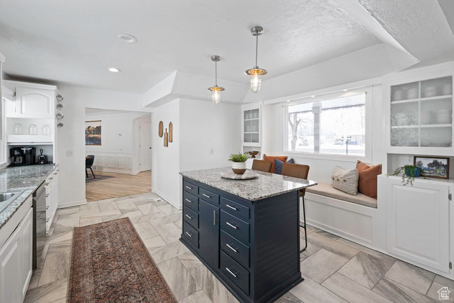 Kitchen with a kitchen island, light wood-type flooring, white cabinets, decorative light fixtures, and dishwasher