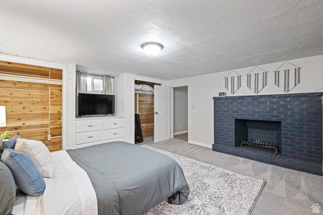 Carpeted bedroom featuring wooden walls, a textured ceiling, and a fireplace