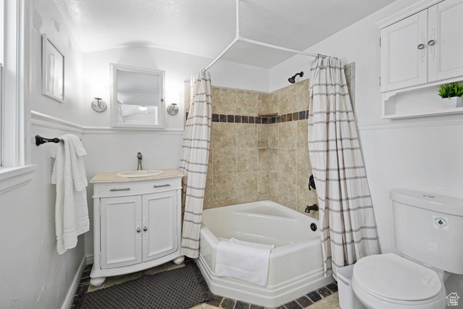 Full bathroom featuring shower / bath combo with shower curtain, vanity, toilet, and tile floors