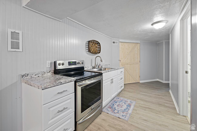 Kitchen featuring stainless steel electric stove, light wood-type flooring, white cabinets, sink, and a textured ceiling