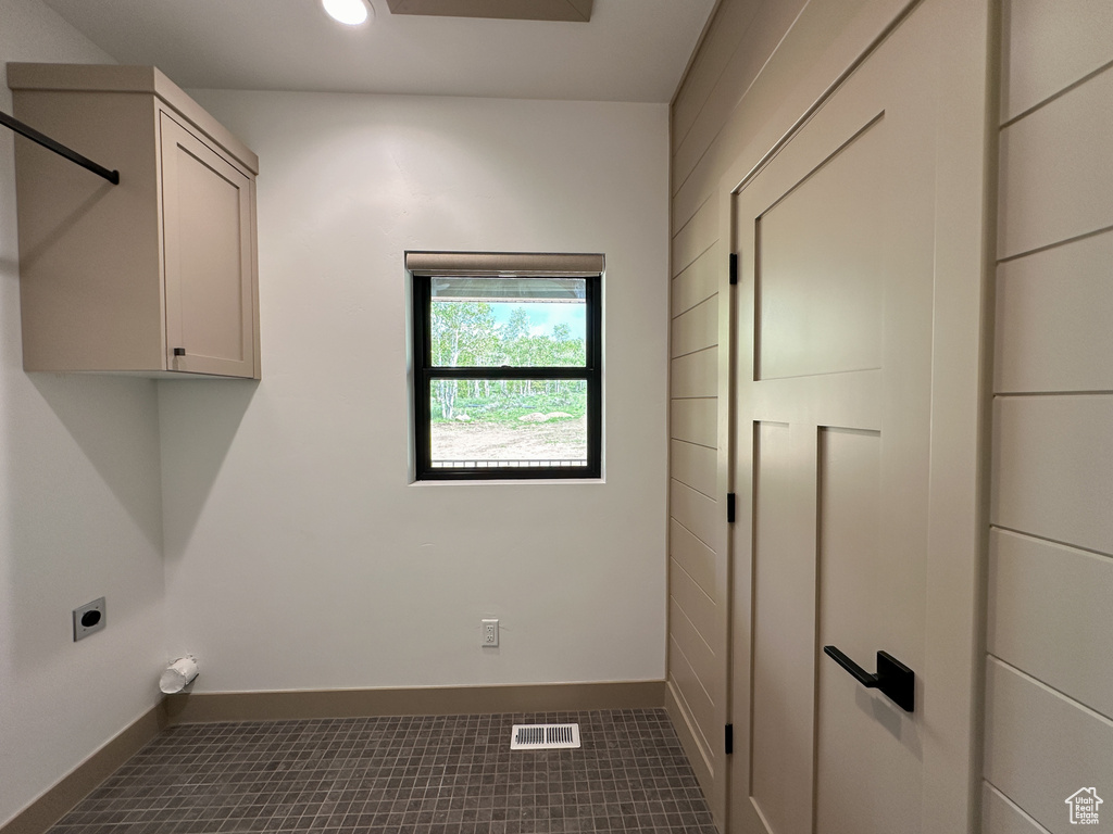 Laundry area with dark tile flooring, electric dryer hookup, and cabinets