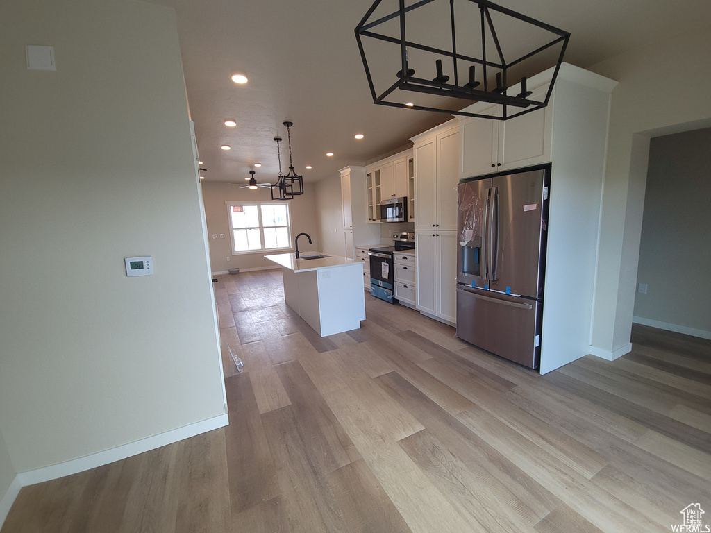 Kitchen featuring appliances with stainless steel finishes, decorative light fixtures, light hardwood / wood-style floors, and a center island with sink