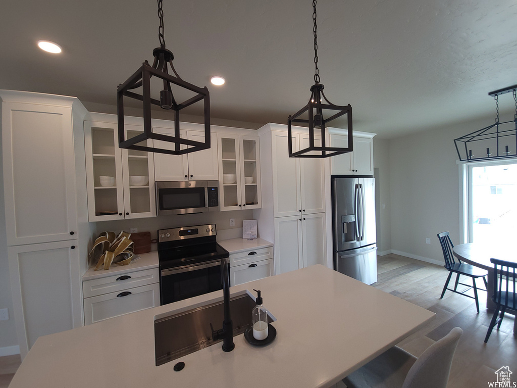 Kitchen with decorative light fixtures, light hardwood / wood-style floors, white cabinetry, and stainless steel appliances