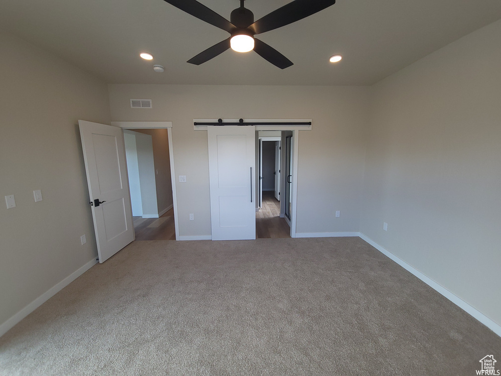 Unfurnished bedroom with a barn door, ceiling fan, and carpet floors