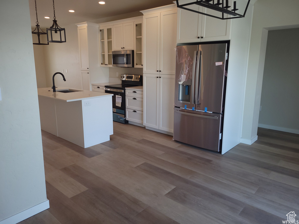 Kitchen featuring hanging light fixtures, appliances with stainless steel finishes, hardwood / wood-style flooring, and white cabinets