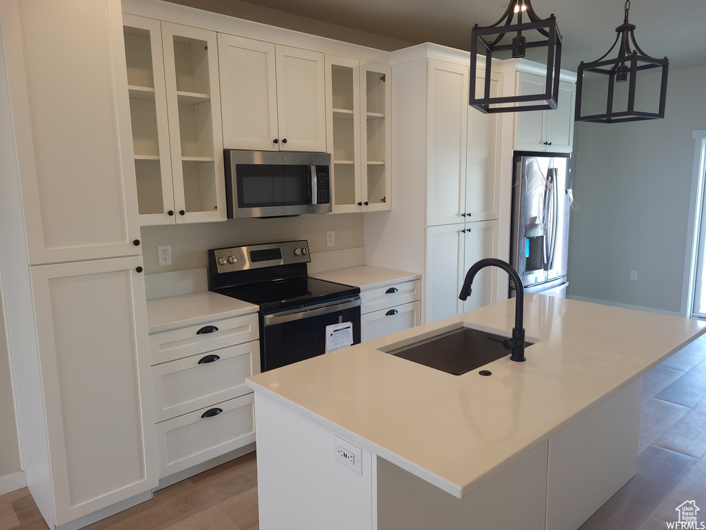 Kitchen with decorative light fixtures, stainless steel appliances, hardwood / wood-style floors, an island with sink, and sink