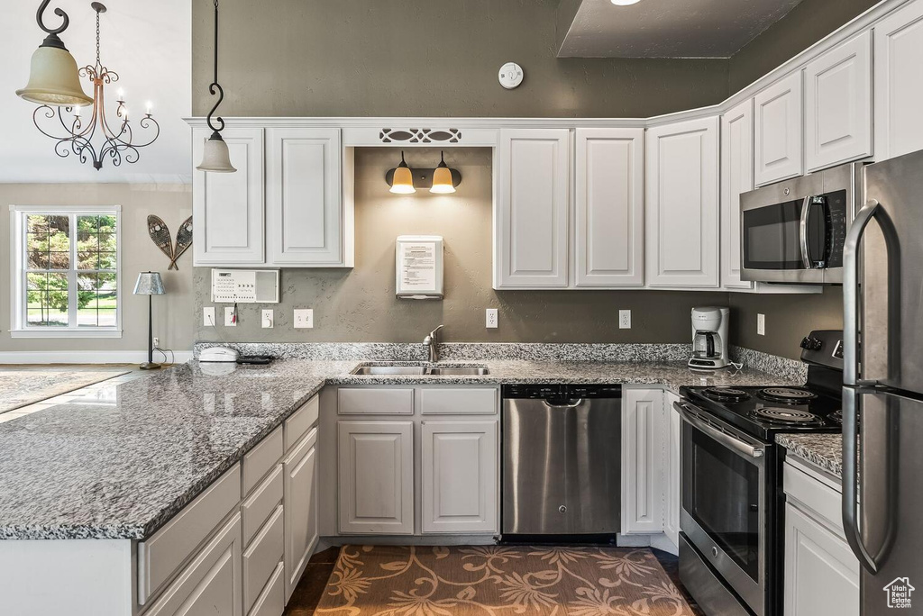 Kitchen with stainless steel appliances, decorative light fixtures, light stone counters, sink, and white cabinets