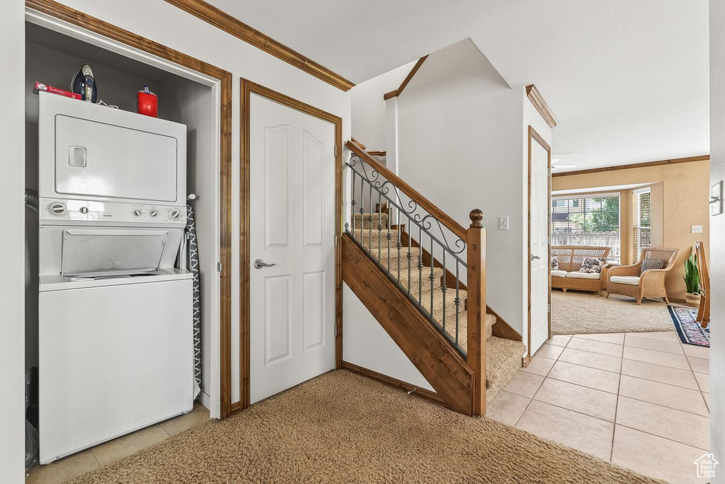 Clothes washing area featuring stacked washer / dryer, light tile floors, and crown molding