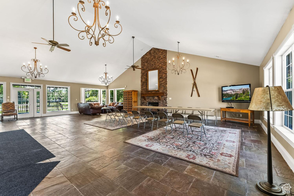 Interior space featuring high vaulted ceiling, dark tile flooring, a large fireplace, and ceiling fan with notable chandelier