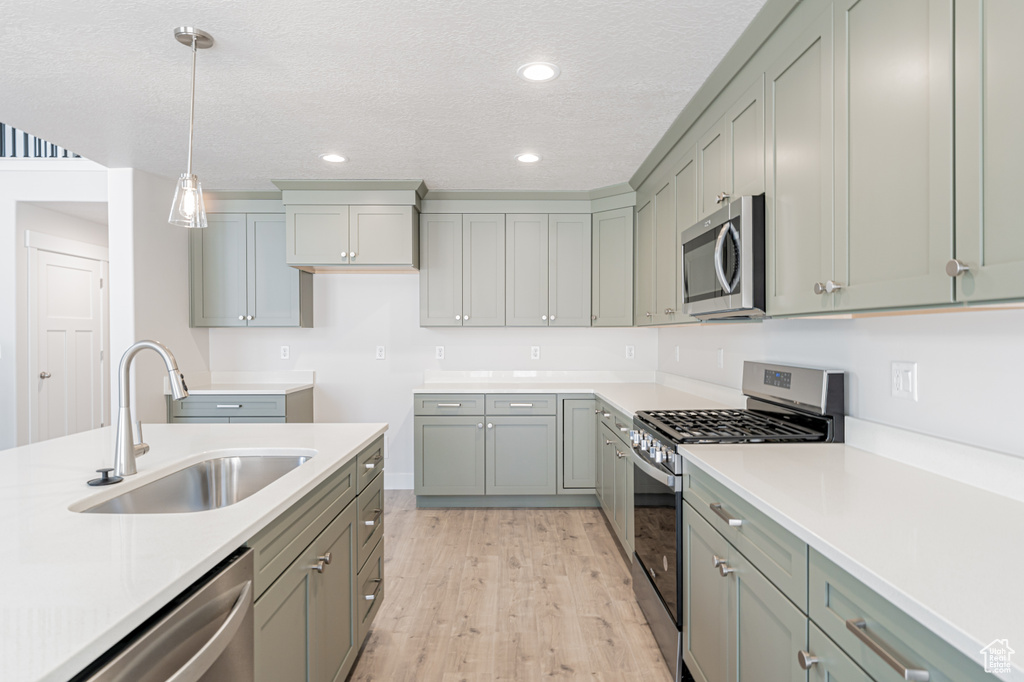 Kitchen with appliances with stainless steel finishes, light hardwood / wood-style floors, a textured ceiling, decorative light fixtures, and sink