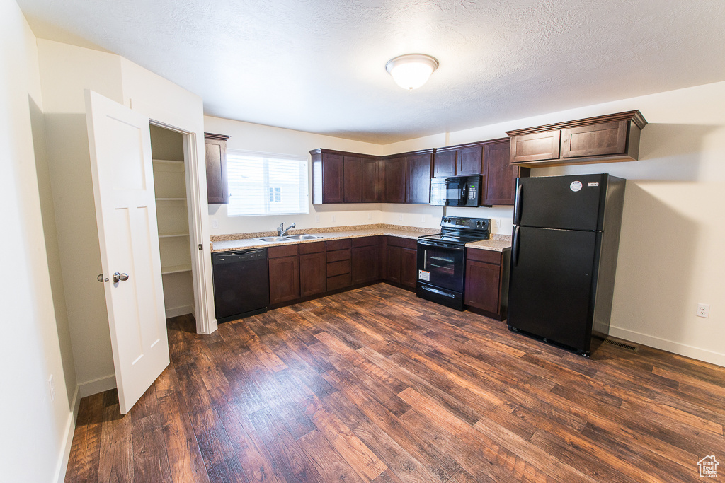 Kitchen with light stone countertops, dark hardwood / wood-style flooring, black appliances, dark brown cabinets, and sink