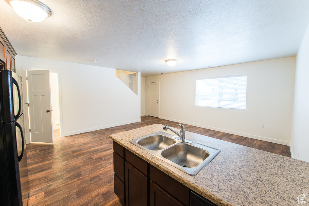 Kitchen with dark brown cabinets, dark wood-type flooring, black refrigerator, a textured ceiling, and sink