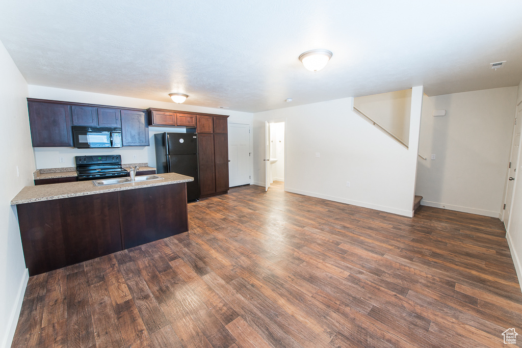 Kitchen featuring light stone counters, dark wood-type flooring, sink, and black appliances