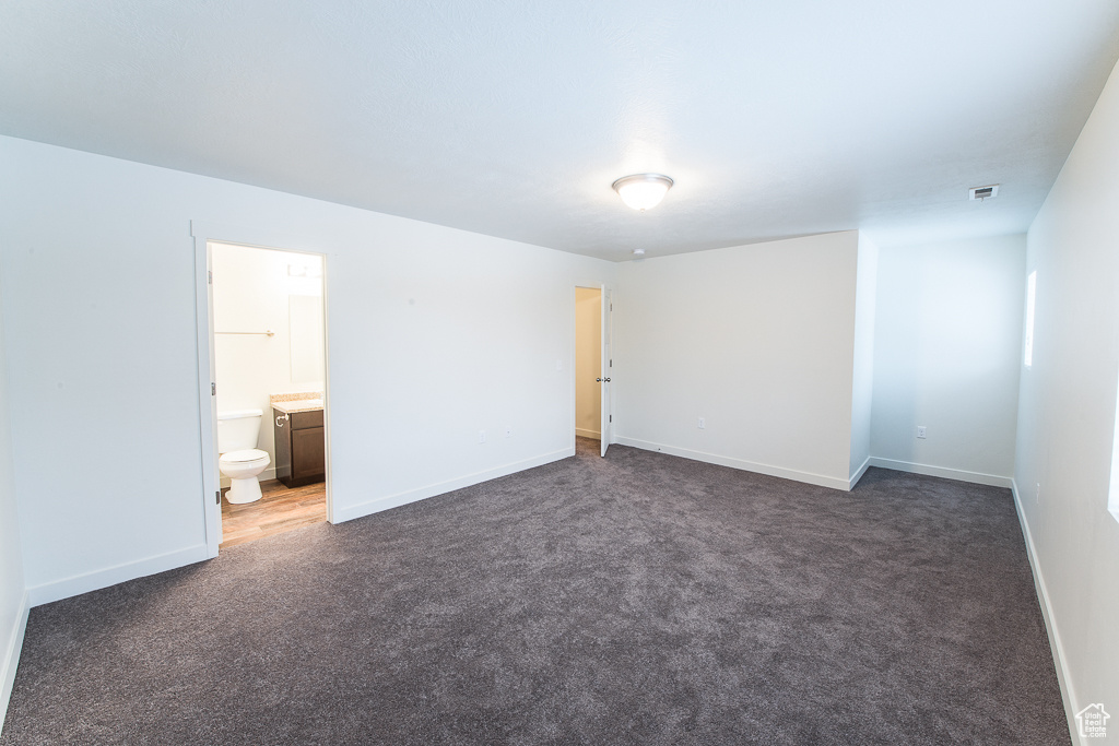 Unfurnished bedroom with connected bathroom and dark carpet