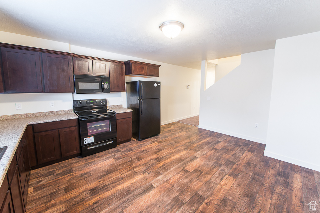 Kitchen featuring dark brown cabinetry, black appliances, and dark wood-type flooring