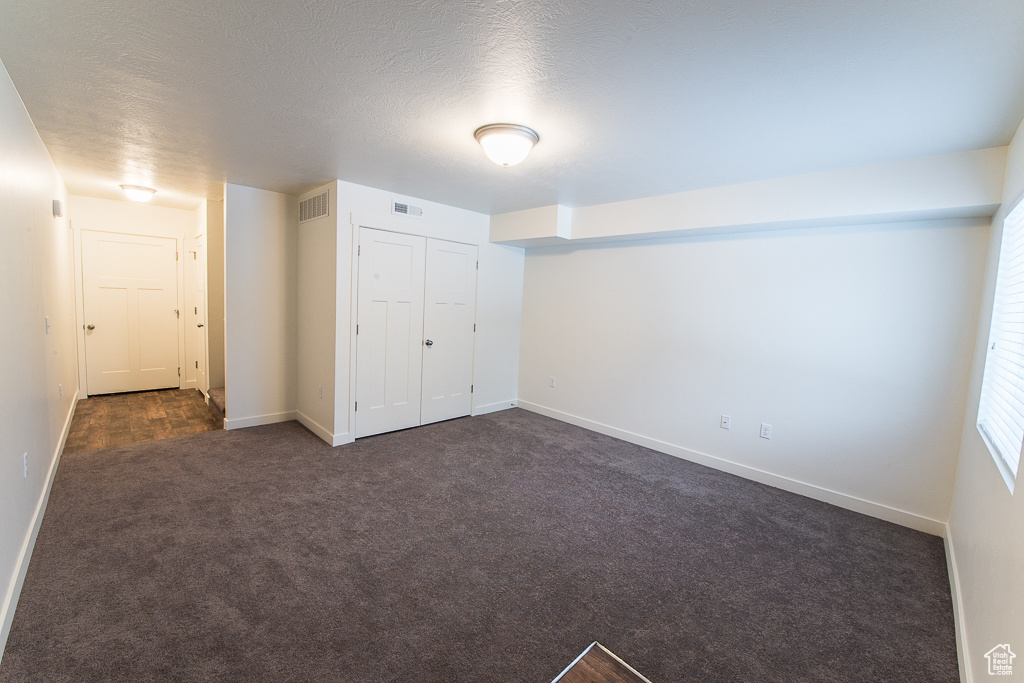 Unfurnished bedroom featuring dark colored carpet, a closet, and a textured ceiling