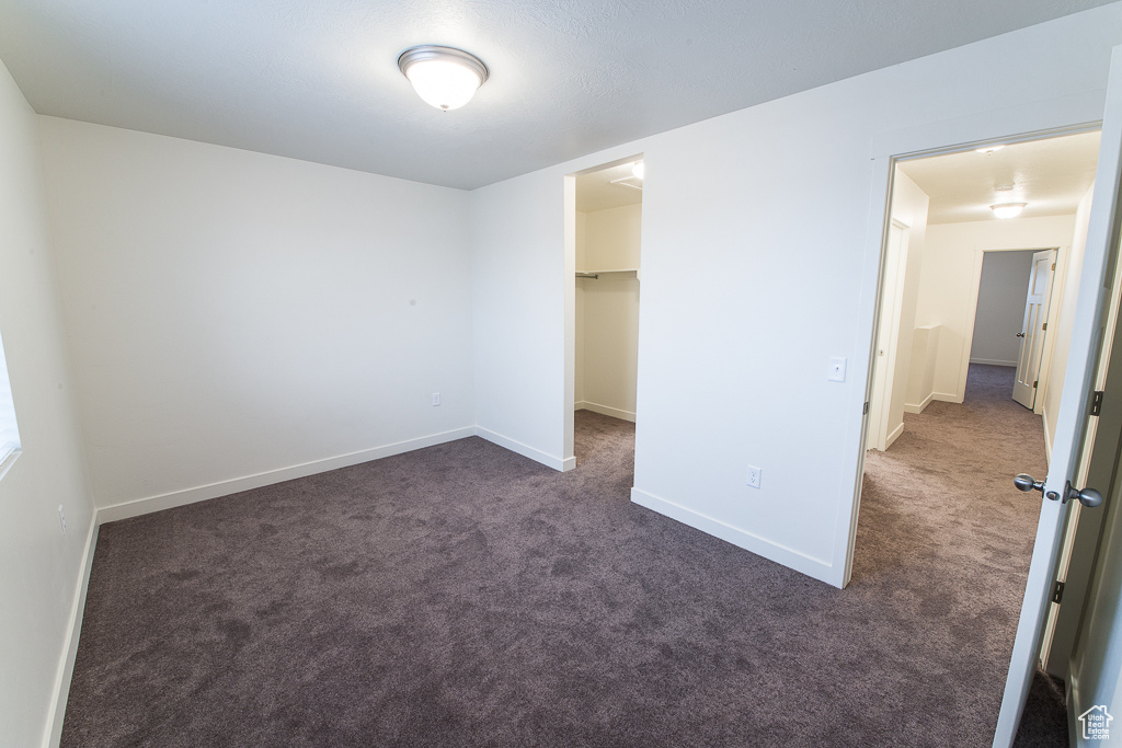 Unfurnished bedroom with a walk in closet, a closet, and dark colored carpet