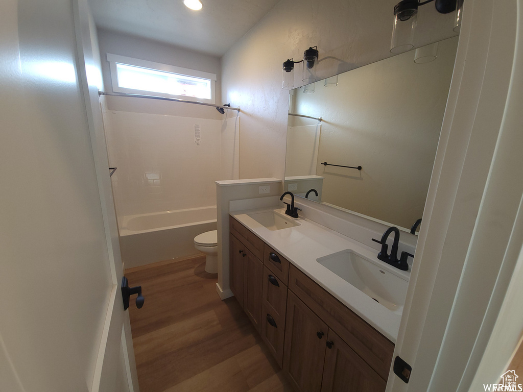 Full bathroom featuring toilet,  shower combination, wood-type flooring, oversized vanity, and dual sinks